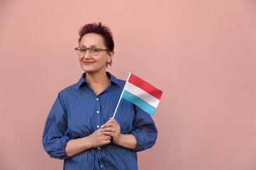 Luxembourg flag. Woman holding Luxembourg flag. Nice portrait of middle aged lady 40 50 years old with a national flag over pink wall background.