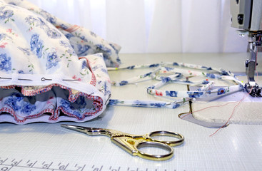 Incomplete colorful cotton dress in blue flowers is fasten with pins on sewing machine