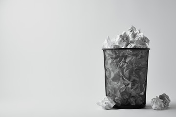 office trash bin with crumpled papers on white surface