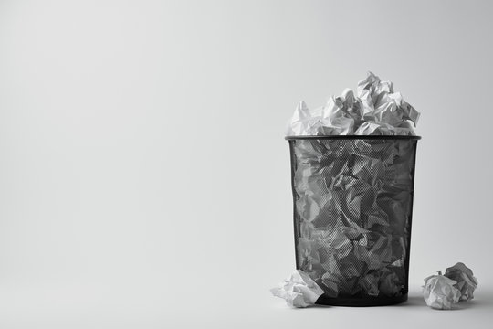 office trash bin with crumpled papers on white surface
