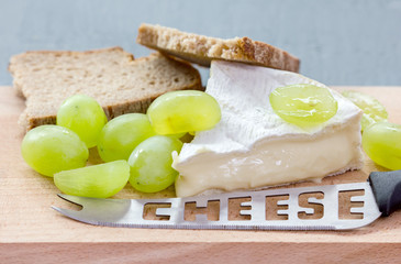 Cheese, grapes, bread and knife lie on a wooden board