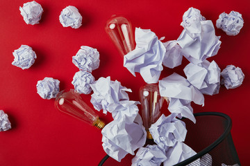 top view of crumpled papers with vintage incandescent lamps spilled from trash bin on red tabletop