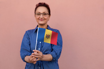 Moldova flag. Woman holding Moldovan flag. Nice portrait of middle aged lady 40 50 years old with a national flag over pink wall background outdoors.