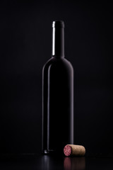 Red wine cork with silhouette of red wine bottle behind isolated on black dark background with soft reflections and beautiful shadows. Shallow depth of field