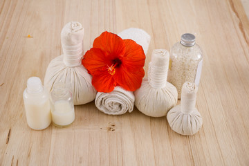 Fototapeta na wymiar red hibiscus with herbal ball, rolled towel with bottle oil - wooden background