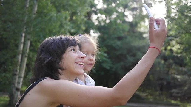 Cute family mother with child daughter taking selfie smart phone photo on nature