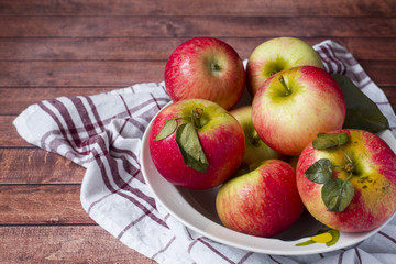 Fresh red apples with green leaves in a plate on a napkin. Dark wooden background.