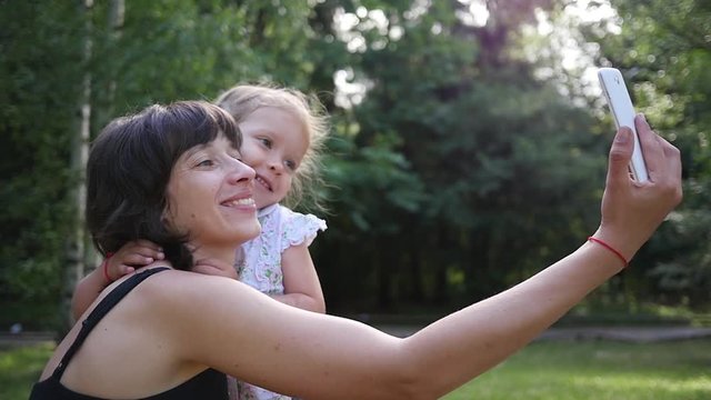 Beautiful happy family mother and little kid daughter hugging kissing shooting selfie photo during walking on nature park