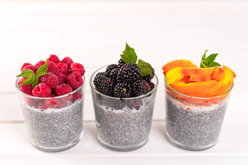 Healthy eating and dieting concept. Homemade white chia pudding with fresh berries and green leaves for breakfast on a light kitchen table. Three glasses, raspberry, blackberry, apricot or peach. 