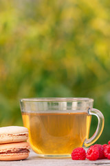 Glass cup of green tea, delicious macaroons cakes of different color and raspberries