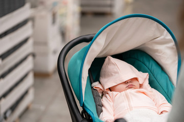 A three-month-old child sleeps in a wheelchair hiding behind a hood in a shopping center.