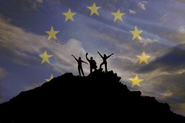 Silhouettes of happy three people on top of a mountain, but the background of the flag of the euro union and sky
