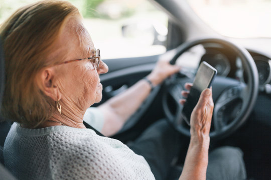 Elderly woman behind the steering wheel using her phone