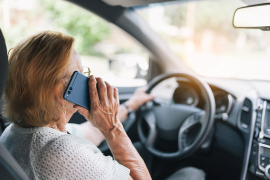 Elderly woman behind the steering wheel using her phone