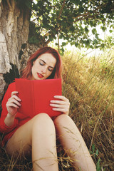 Mujer joven y pelirroja leyendo un libro al aire libre 