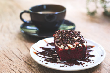 A piece of red velvet cake with coffee cup on wooden table in cafe