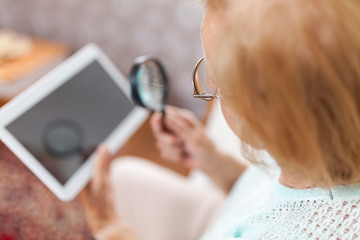 Elderly woman with glasses and loupe using a digital tablet