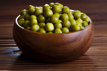 Green peas in a wooden bowl on dark brown wooden table