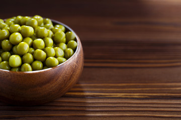 Green peas in a wooden bowl on dark brown wooden table