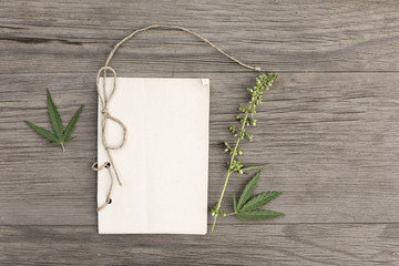 Hemp leaves and flowers with handmade craft notebook on old grunge wooden background. Top view. Minimalistic mockup.