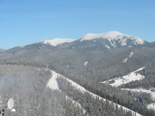 Beautiful winter carpathies with snowy peaks, ski slopes, fir trees and blue sky
