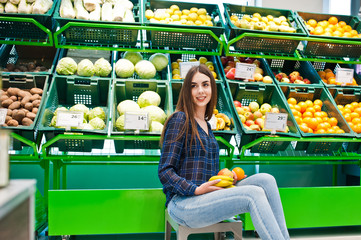Shopping woman looking at the shelves in the supermarket.  Portrait of a young girl in a market store at fruits and vegetables section.