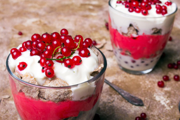Healthy dessert with organic red currants, fresh yogurt and corn flakes. Dietary breakfast on a brown background