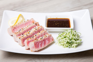 Grilled tuna with sesame seeds and cucumber salad on a white plate. Close-up, selective focus