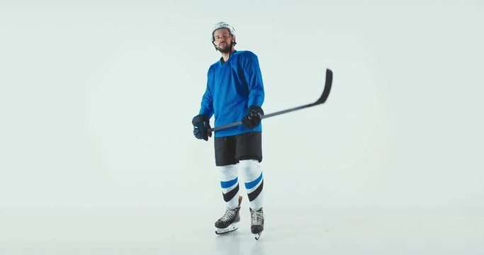 Portrait of Caucasian male ice hockey player in uniform pointing a stick into camera against white background. Studio shot. 4K UHD 60 FPS SLOW MOTION