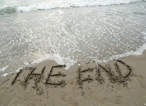 big text THE END that is deleted by the sea wave on the beach