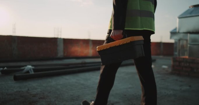 Closeup construction site builder or engineer walking to see amazing sunset holding a instrument bag wearing a safety vest.