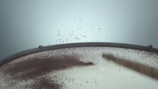 Brown holi powder bounces off drum in shockwave pattern.