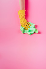 partial view of female cleaner wiping dust by rag, pink background