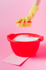 cropped image of female cleaner holding washing sponge over plastic basin with foam, pink background