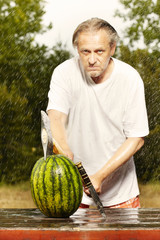 Naklejka na ściany i meble Man slicing watermelon in summer rainy day with double axe