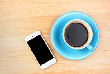 Fototapeta na wymiar Blue and white coffee cup and smartphone with blank screen on wooden table background.
