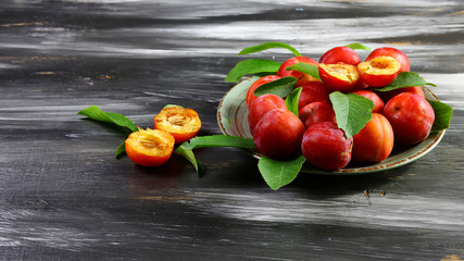 Fresh red plums with leaves on a ceramic plate. On a dark background. Free space for text. Flat lay