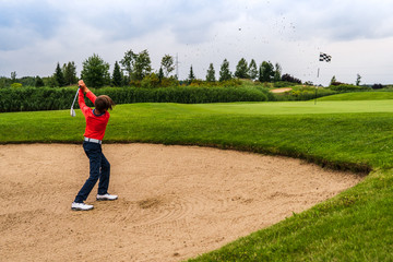 Boy golf player chipping from sand bunker onto green
