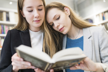 Portrait of two teenage girls reading book together in a public library
