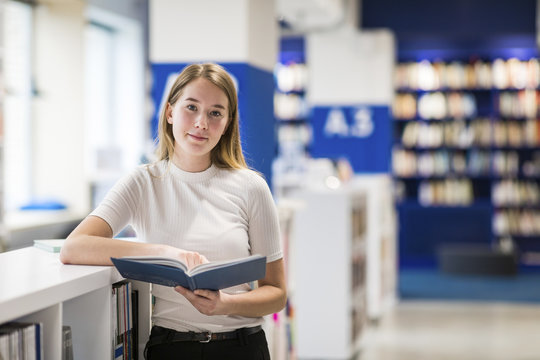 Portrait of relaxed teenage girl with book in a public library