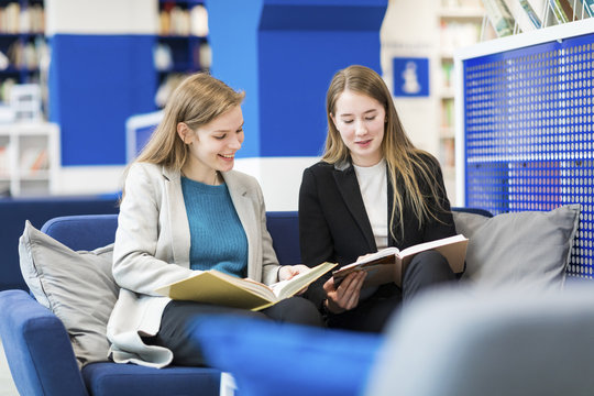 Two teenage girls sitting on couch in a public library reading books