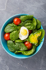 Healthy food concept. Salad in blue bowl on dark background. Avocado, tomato, spinach, egg. Diet concept. Top view. close-up.