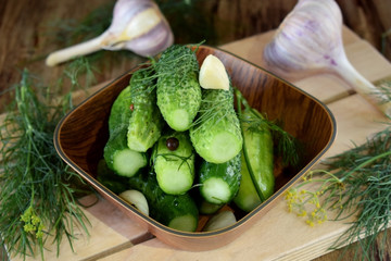 Light-salted cucumbers in a wooden bowl surrounded by the ingredients. Traditional Russian cuisine snack