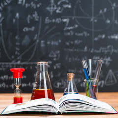 School supplies. Tubes with chemical liquids stand on a wooden table on a chalkboard background