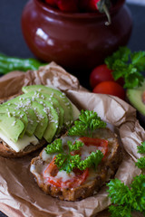 Useful delicious sandwiches - whole wheat bread, tomatoes, avocado and cheese on a background of paper and a pot of pepper. Vegetarian food.