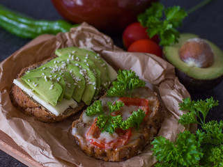 Useful delicious sandwiches - whole wheat bread, tomatoes, avocado and cheese on a paper background. Vegetarian food.