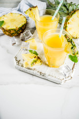 Fresh pineapple juice or cocktail, with pieces of fresh pineapple, ice, decorated with mint, on a white marble table, copy space