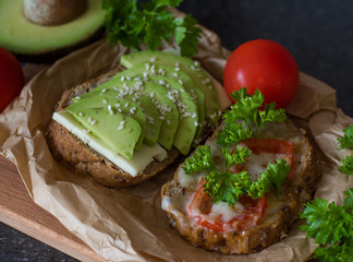 Useful delicious sandwiches - whole wheat bread, tomatoes, avocado and cheese on a paper background. Vegetarian food.