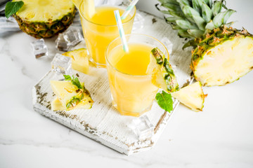 Fresh pineapple juice or cocktail, with pieces of fresh pineapple, ice, decorated with mint, on a white marble table, copy space