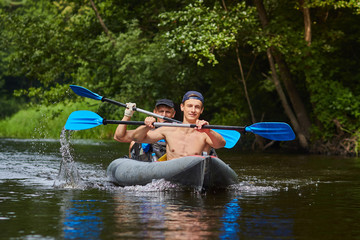 Rowers with oars in a canoe on rafting along the river in a summer sunny day. Friends are swimming...
